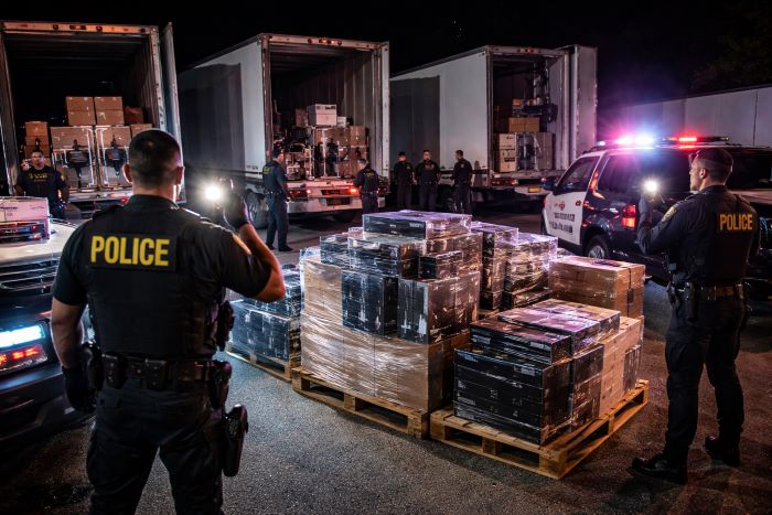 Florida police officers inspecting recovered cargo and pallets of boxed goods during a nighttime freight theft operation.